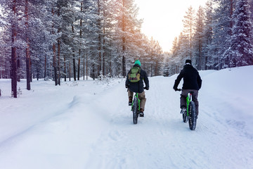 two people with fat bikes riding snowy winter forest trail in finland