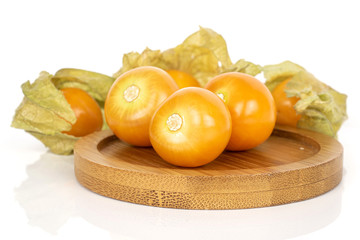 Group of six whole fresh orange physalis on round bamboo coaster isolated on white background