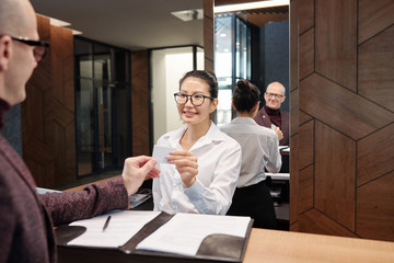 Happy young businesswoman taking card from hotel room after filling in form