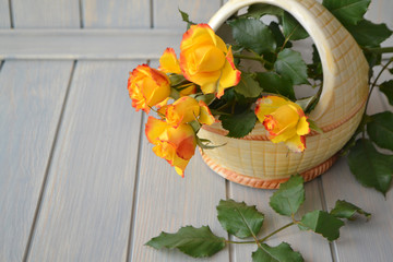 Bright orange and yellow little roses in a ceramic basket on blue wooden background