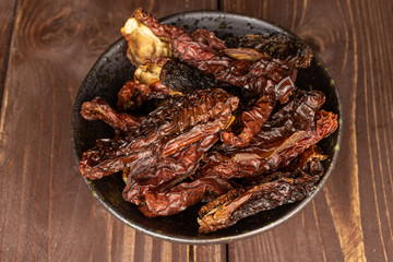 Lot of whole dried red tomato piece in glazed bowl flatlay on brown wood