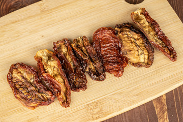 Group of seven whole dried red tomato piece on bamboo cutting board flatlay on brown wood