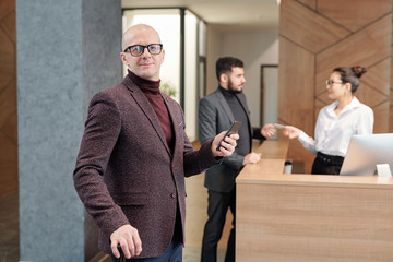 Bald elegant mature male business traveler waiting for taxi in hotel lounge