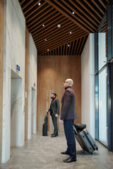 Two traveling businessmen with suitcases waiting for elevator in hotel
