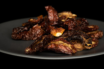 Lot of whole dried red tomato piece on gray ceramic plate isolated on black glass