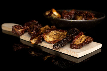 Lot of whole dried red tomato piece on wooden cutting board in glazed bowl isolated on black glass