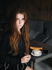 Cute redhead woman woman with serious facial expression sitting in cozy city cafe enjoying free time coffee break with cappuccino and dessert