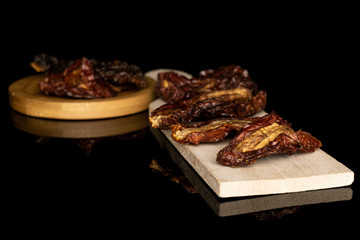 Lot of whole dried red tomato piece on wooden cutting board on round bamboo coaster isolated on black glass