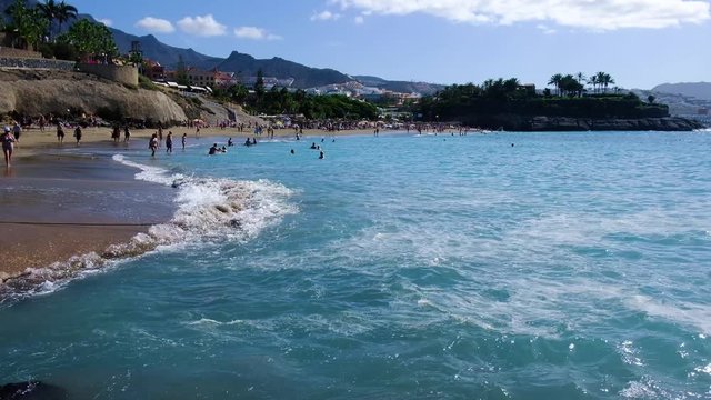 COSTA ADEJE, TENERIFE, SPAIN - NOVEMBER 2019: People lay on the sand and swim in the ocean at tropical beach.