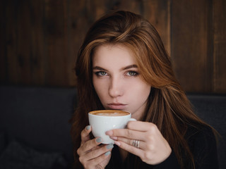 Close up headshot beautiful caucasian red haired woman holding mug drinking cappuccino coffee with latte art adorable smile and feeling good in trendy city cafe