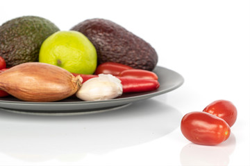 Lot of whole fresh ingredient guacamole on gray ceramic plate isolated on white background