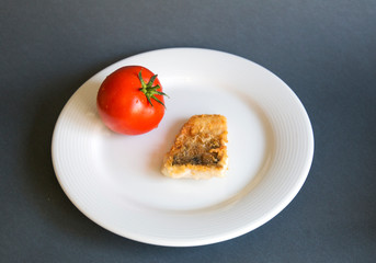  On a plate a slice of fish whole tomatoes