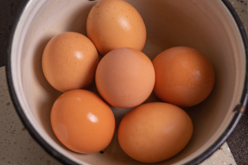 Boiled brown eggs lie in a white enamel pan.