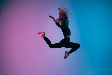 Sporty girl in charismatic jump moment against trendy color background. Young fit dancer woman jumping. Studio shot