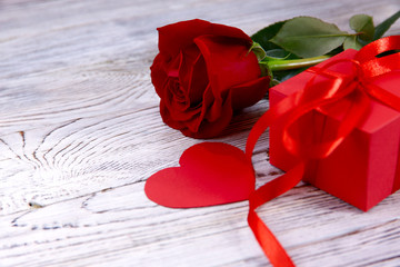 Valentine's day background. On a gray wooden background on the right is a red gift, a red heart and a red rose. Close-up, horizontal, side view, free space for text.