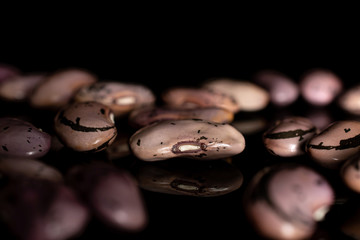 Lot of whole fresh speckled bean pinto isolated on black glass
