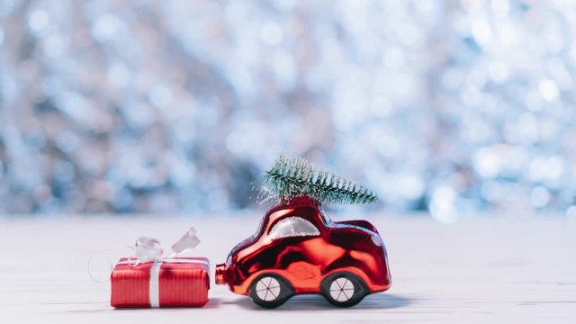 Stop motion, little red toy car carries a Christmas tree on a blue blurred background