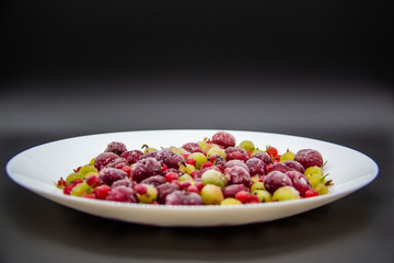 Frozen berries from the freezer. Plate with frozen cherries, currants and gooseberries. Healthy berry on a white plate.