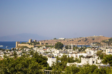 Fototapeta na wymiar Panoramic view on Bodrum downtown with traditional white cubic buildings, green trees and mountains on background. Aegean style, Bodrum town, Mugla, Turkey.