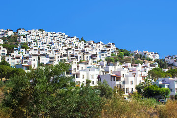 Obraz premium Panoramic view on Bodrum downtown with traditional white cubic buildings, green trees and mountains on background. Aegean style, Bodrum town, Mugla, Turkey.