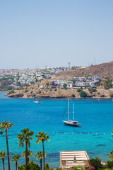 Obraz premium Beautiful view on turquoise Aegean sea with yacht and pontoon that moored on the seashore with sunbeds and umbrellas near luxury Turkish hotel in Akyarlar region of Bodrum, Turkey. Turkish vacation.