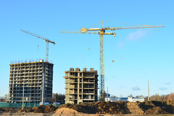 Tower cranes constructing a new residential building at a construction site against blue sky. Renovation program, development, concept of the buildings industry.