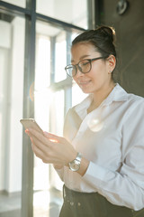 Young Asian businesswoman in formalwear and eyeglasses looking through contacts