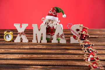 Wooden letters forming word XMAS with ribbons and red figures of dolls besides them. the doll climbs the rope ladder to letters