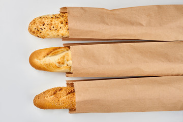 Set of fresh baguettes on white background. Three baguettes in kraft paper bags. Food at grocery.