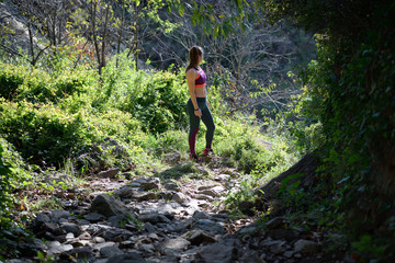 Sportswoman rests and looks at the horizon in a beautiful natural environment with a mountain path full of rocks while doing his daily training