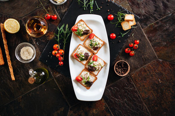 Brushetta set. Variety of small sandwiches with egg, tuna, arugula and salad served with glass of cognac on a black stone board over dark background