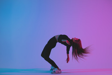 Sporty woman dancing in studio against colorful phantom blue color background. Young athletic girl dancer posing