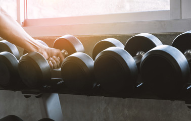 Man's hand picked the dumbbell on dumbbell rack for exercise at gym fitness background.