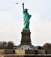 Obraz premium The Statue of Liberty view from water with passenger plane on background