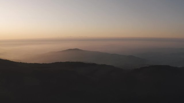 Aerial view of the misty mountains. Fly over sunset clouds and hills.