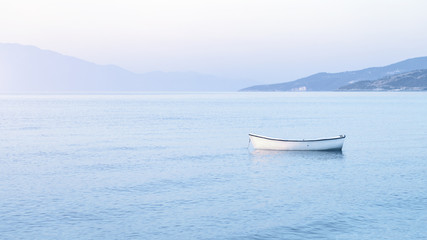 Tender shades of pastel blue morning haze color sunrise with white boat at anchor in blue waters. Travel and vacation destination concept or peace and tranquility concept banner with copy space