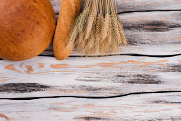 Bread and wheat ears on wooden background. Bunch of wheat ears and freshly baked bread. Copy space.