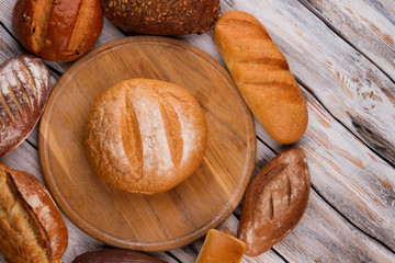 Bread on wooden kitchen cutting board. Different types of bread on rustic wooden background.