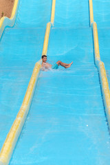 Happy European boy having fun in aqua park, he gliding down colorful slide.