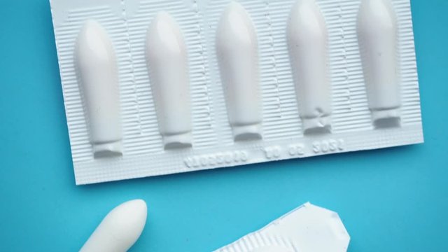 White suppositories for anal or vaginal use on a blue table and a thermometer with a temperature of 38 degrees. Medical candles for treatment of Candida, thrush, hemorrhoids, inflammation and fever