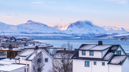 Tromso, Norway. View of the arctic city with traditional wooden houses in winter, snowy mountains in the background.