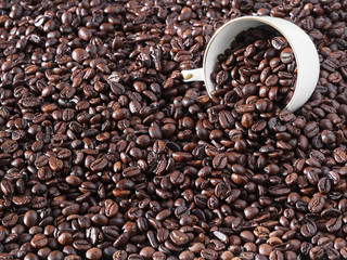 Roasted coffee beans, background. Horizontal orientation. Fresh aromatic dark coffee. A white cup for espresso lies in the beans. Close-up, selective focus on grains.