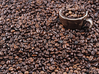 Roasted coffee beans, background. Horizontal orientation. Fresh aromatic dark coffee. A brown cup for espresso stands in coffee beans. Close-up. Selective focus on a cup with coffee grains.