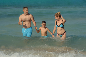 Mother, father and son spending time on sea beach on summer vacations. They are coming out of water.