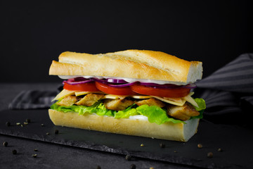 Food photography of a grilled chicken sandwich with tomatoes and red onions on baguette bread on a black background