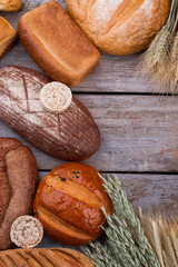 Obraz na płótnie Canvas Assortment of rustic bread on wooden background. Bread loaves and wheat ears, top view. Space for text.