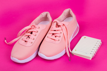 Sneakers and notebook. Doing sports on a pink background.