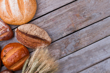 Various bread loaves and wheat ears. Homemade crusty bread on old wooden background with copy space.