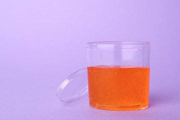 Orange slime in plastic container on violet background. Space for text