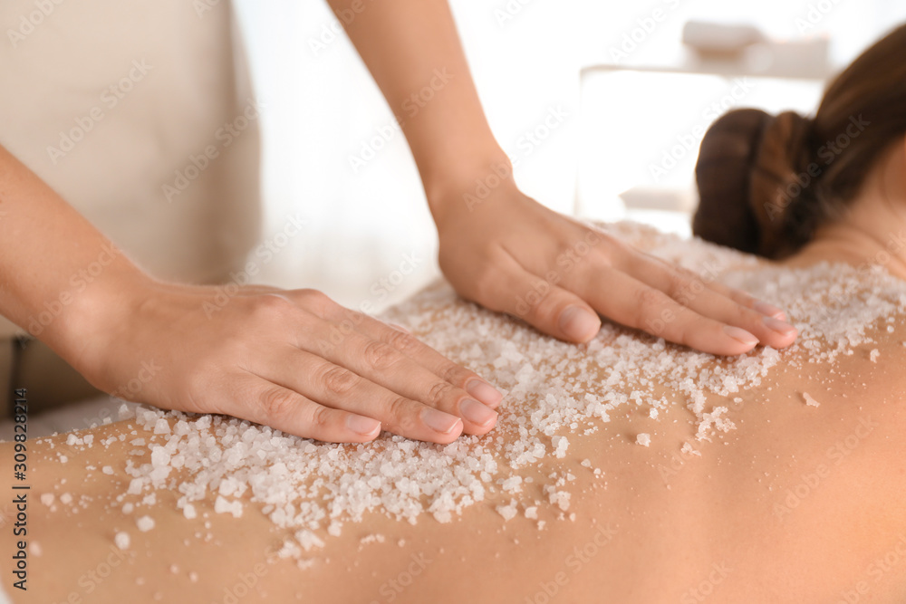 Poster Young woman having body scrubbing procedure with sea salt in spa salon, closeup